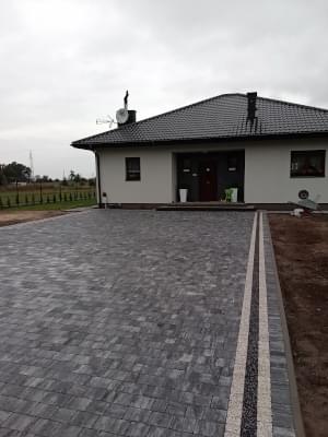 Szara kostka z białym paskiem ułożona przed drzwiami tarasowymi domu